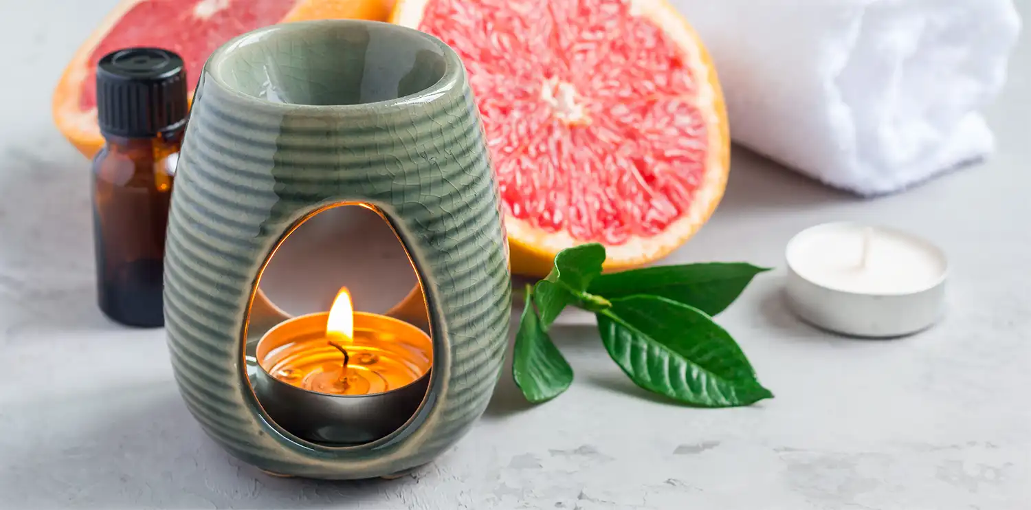 A candle diffuser next to a freshly sliced grapefruit and a bottle of grapefruit essential oil